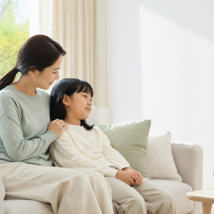 평촌 환절기 기관지염 – 엄마가 소파에 함께 앉은 여자아이의 어깨에 손을 얹고 아이가 엄마에게 기대어 쉬는 모습